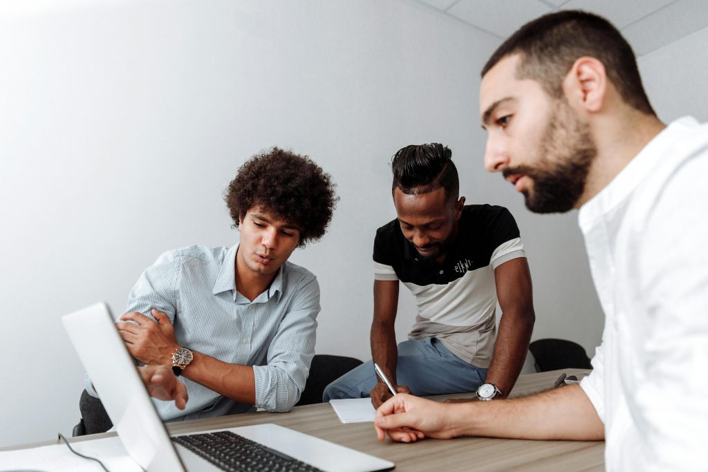 Diverse group of young men collaborating in an office meeting room with a laptop.
